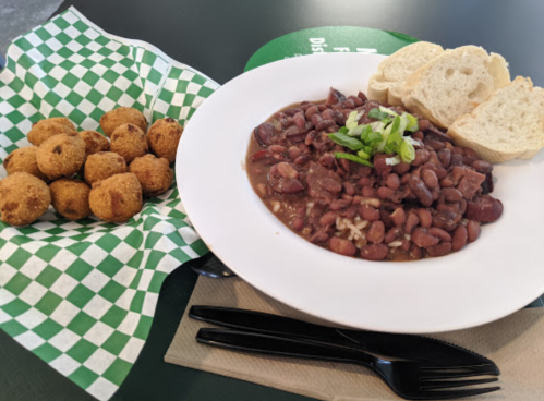 A bowl of red beans with rice and green onions, served with cornbread balls and slices of bread on a green checkered tray.