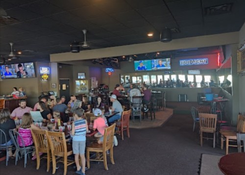 A busy restaurant interior with families dining, a bar area, and multiple TVs showing sports.