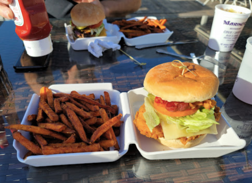 A crispy chicken sandwich with lettuce, tomato, and cheese, served with a side of sweet potato fries on a table.
