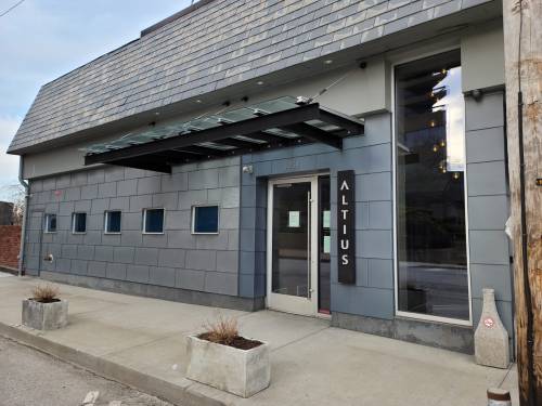 Exterior of a modern building with a gray facade, featuring a sign that reads "ALTITUS" and large windows.