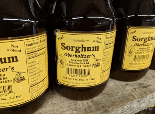 Bottles of Oberholtzer's sorghum syrup with yellow labels, displayed on a wooden shelf.
