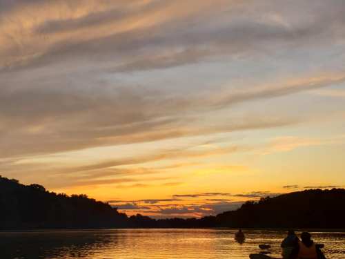 A serene sunset over a calm lake, with silhouettes of kayakers enjoying the view.