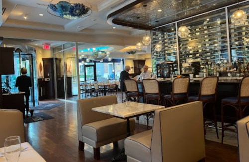 A stylish restaurant interior featuring a bar, tables, and wine display, with patrons dining and staff serving.
