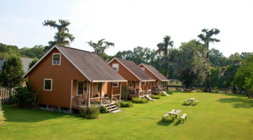 Four orange cabins with porches on a grassy area, surrounded by trees and picnic tables under a clear blue sky.