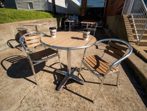 A round table with two metal chairs, each holding a coffee cup, set on a concrete patio.