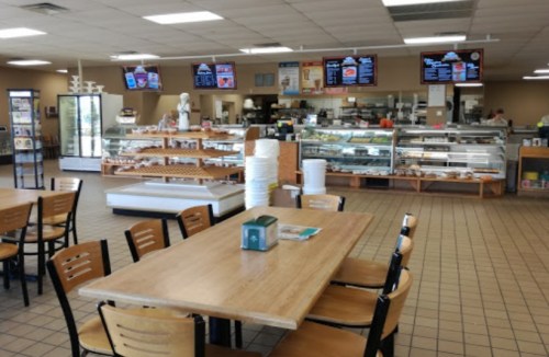 A spacious café interior with tables, a display case of pastries, and digital menus on the wall.