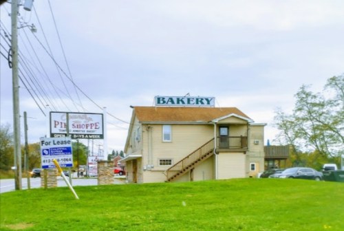 A two-story building with a sign reading "BAKERY" and a "For Lease" sign in front, set on a grassy area.