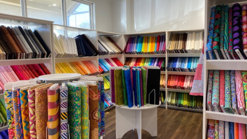 A vibrant fabric store showcasing colorful rolls of fabric arranged on shelves and a display stand in the center.