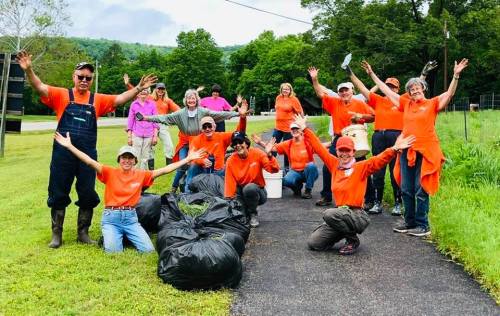 A group of volunteers in orange shirts cheerfully pose with trash bags after a cleanup event in a green park.