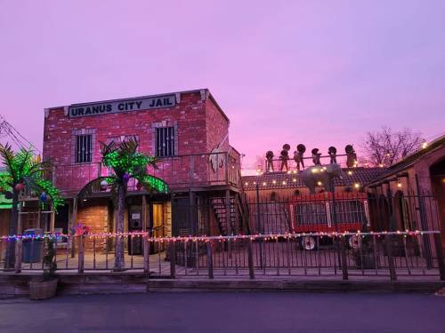 A whimsical jail building with colorful lights, palm trees, and a pink sky at dusk.