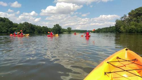 A group of kayakers paddles on a calm river under a partly cloudy sky.