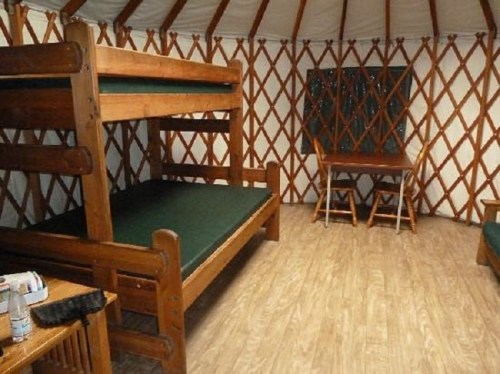 Interior of a yurt featuring wooden bunk beds, a table with chairs, and a wooden floor.