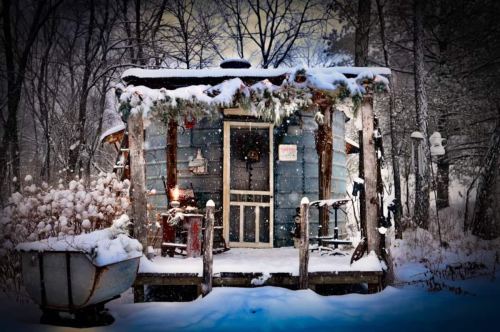A cozy, snow-covered cabin surrounded by trees, with festive decorations and a rustic porch.