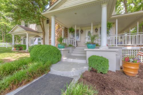 A charming porch with white columns, potted plants, and a landscaped pathway leading to a welcoming entrance.