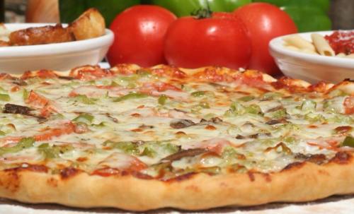 A close-up of a freshly baked pizza topped with green peppers, cheese, and tomatoes, with side dishes in the background.