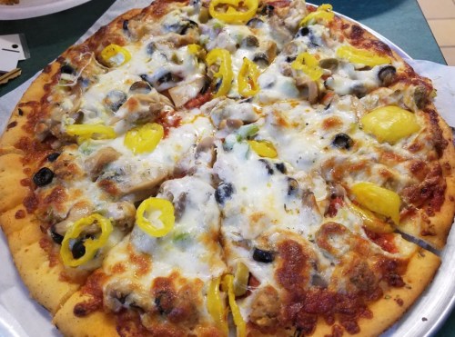 A close-up of a pizza topped with cheese, mushrooms, olives, green peppers, and yellow peppers on a golden crust.