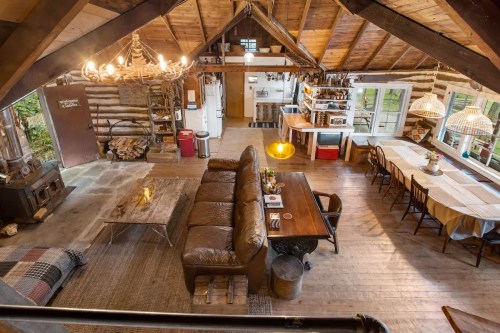 Cozy cabin interior with wooden beams, a large sofa, dining table, and a warm, inviting atmosphere.