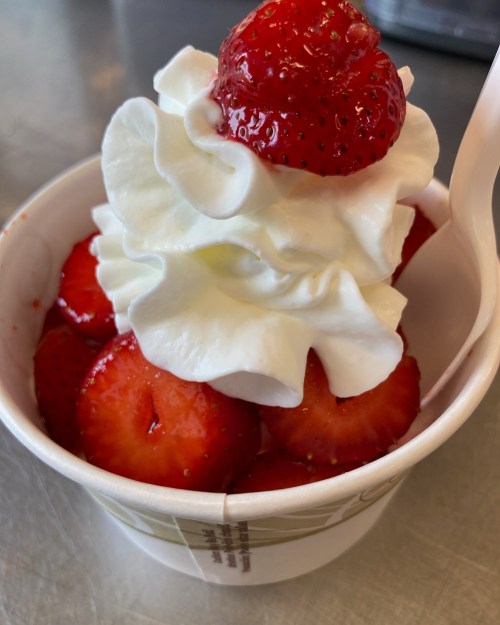 A cup of fresh strawberries topped with whipped cream and a whole strawberry on top.