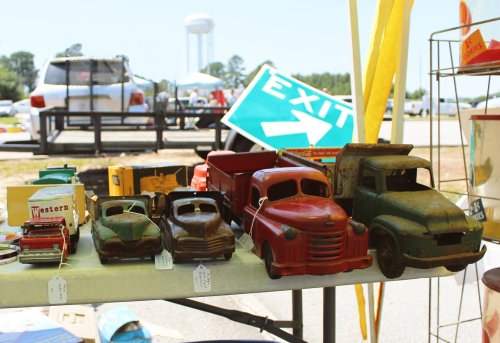 A display of vintage toy trucks and cars on a table at an outdoor market, with a water tower in the background.