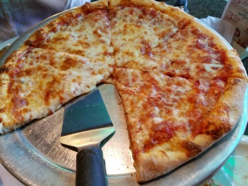 A pizza with several slices cut, resting on a metal tray with a pizza cutter beside it.