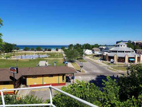 A sunny view of a park, lake, and nearby buildings from an elevated perspective. Clear blue sky above.