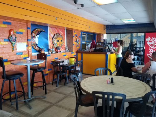 Colorful restaurant interior with vibrant murals, tables, and a counter. Customers are seated and ordering.