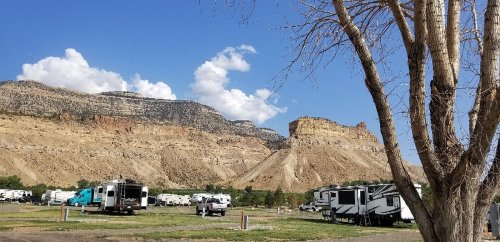 A scenic view of a campground with RVs, surrounded by rocky cliffs and a clear blue sky.