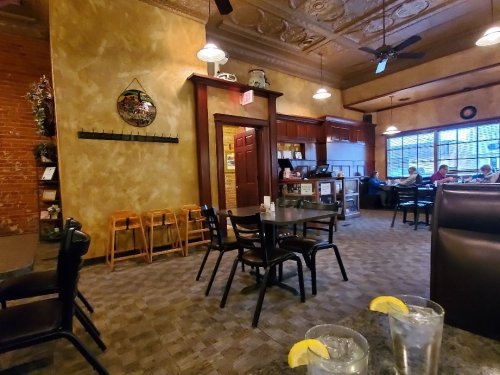 Cozy restaurant interior with wooden furniture, a bar area, and patrons in the background. Two glasses of water on the table.