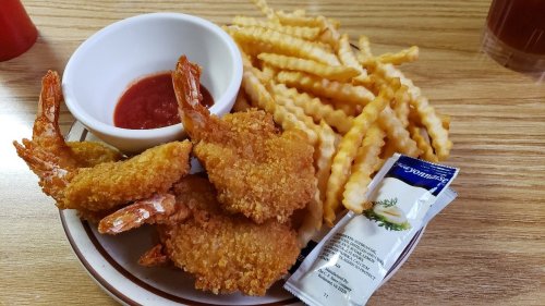 A plate with crispy fried shrimp, crinkle-cut fries, a small bowl of dipping sauce, and a packet of mayonnaise.