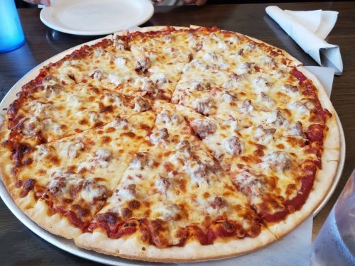 A large pizza with melted cheese and sausage, sliced into equal pieces, on a round tray.