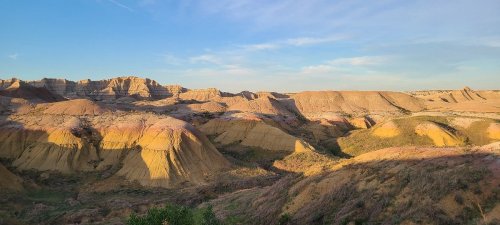 A panoramic view of colorful, layered hills under a clear blue sky, showcasing the natural beauty of a desert landscape.