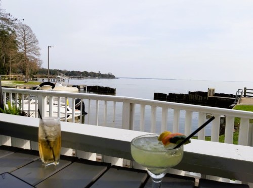 A scenic view of a calm lake with boats, featuring a cocktail and a glass of iced tea on a table.