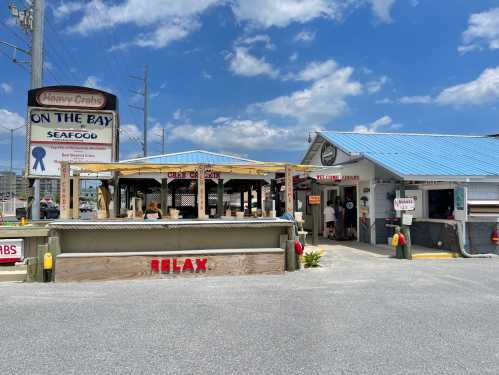 A seafood restaurant with outdoor seating, blue roof, and a sign reading "Heavy Crabs On The Bay" under a sunny sky.