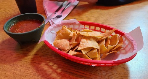 A red basket filled with tortilla chips next to a small bowl of salsa on a wooden table.