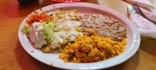 A plate of enchiladas topped with cheese, served with rice, refried beans, lettuce, tomato, and sour cream.
