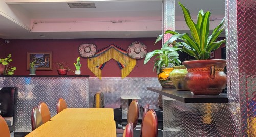 A colorful restaurant interior featuring plants, decorative pottery, and vibrant wall art with a cozy dining area.