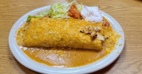 A large cheese-covered burrito with chicken, served with lettuce, tomatoes, and sour cream on a plate.