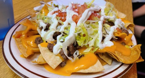 A plate of nachos topped with melted cheese, ground beef, lettuce, tomatoes, and sour cream.