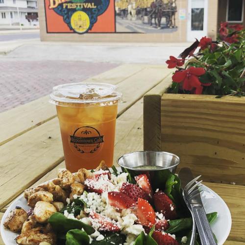 A refreshing iced drink beside a salad with chicken, strawberries, and feta, set against a colorful festival mural.