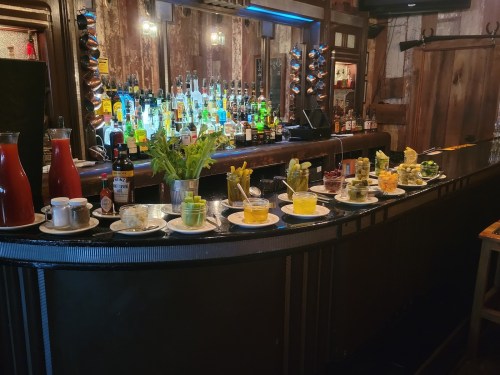 A bar counter with various colorful cocktails and garnishes, set against a backdrop of shelves filled with liquor bottles.