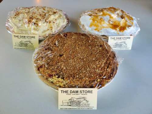 Three pies wrapped in plastic, labeled "The Dam Store," featuring a crumb topping and creamy fillings.