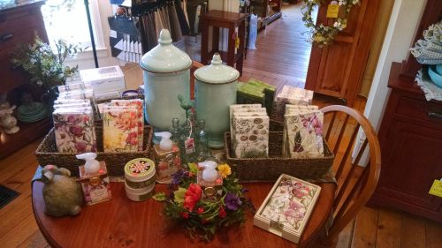 A wooden table displays decorative items, including floral napkins, jars, and a small flower arrangement.