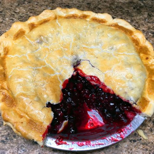 A freshly baked pie with a golden crust and a slice removed, revealing a rich, dark berry filling.