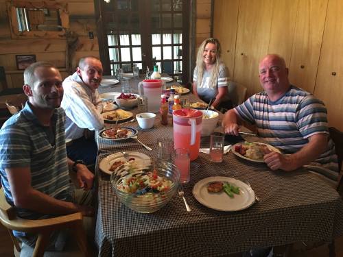 A group of four people enjoying a meal together at a wooden dining table, with various dishes and drinks.