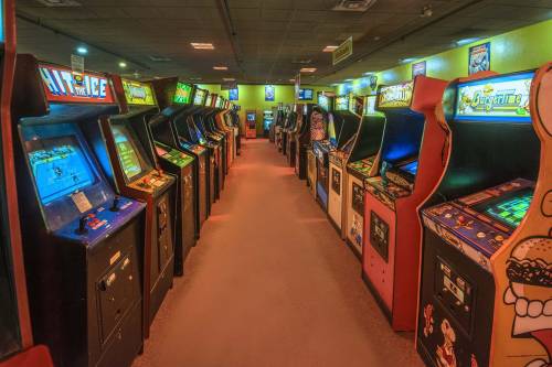 A row of vintage arcade game machines in a brightly lit arcade, showcasing colorful screens and classic designs.