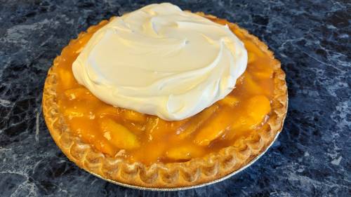 A peach pie topped with a swirl of whipped cream on a blue marble surface.