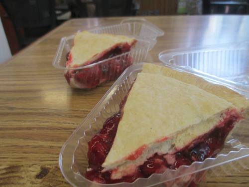 Two slices of cherry pie in clear plastic containers on a wooden table.