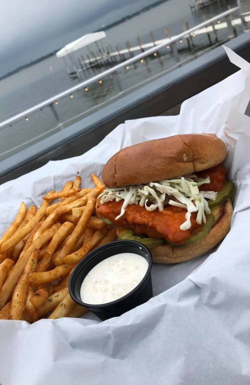 A crispy chicken sandwich with lettuce and pickles, served with a side of golden fries and ranch dressing, by a lake.