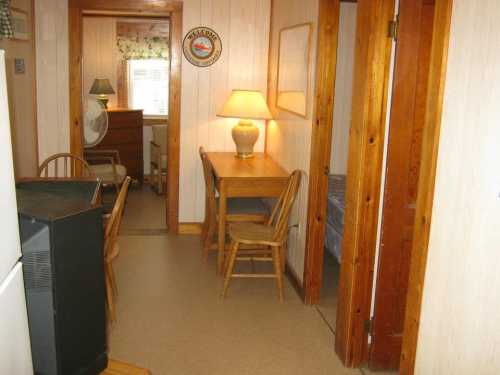 A cozy interior with wooden doors, a table and chairs, a lamp, and a glimpse of a bedroom in the background.