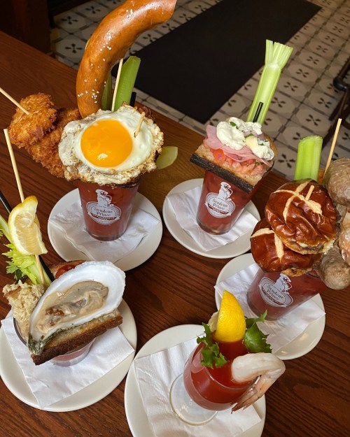 A variety of elaborate Bloody Mary cocktails topped with unique garnishes like fried eggs, pretzels, and seafood.